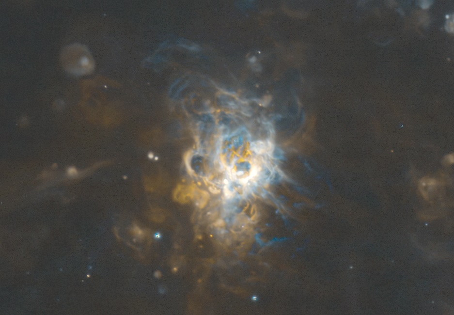 A color image of a nebula. Parts of the nebula are in blue and orange. Numerous loops, bubbles, and filamentary structures can be seen. 